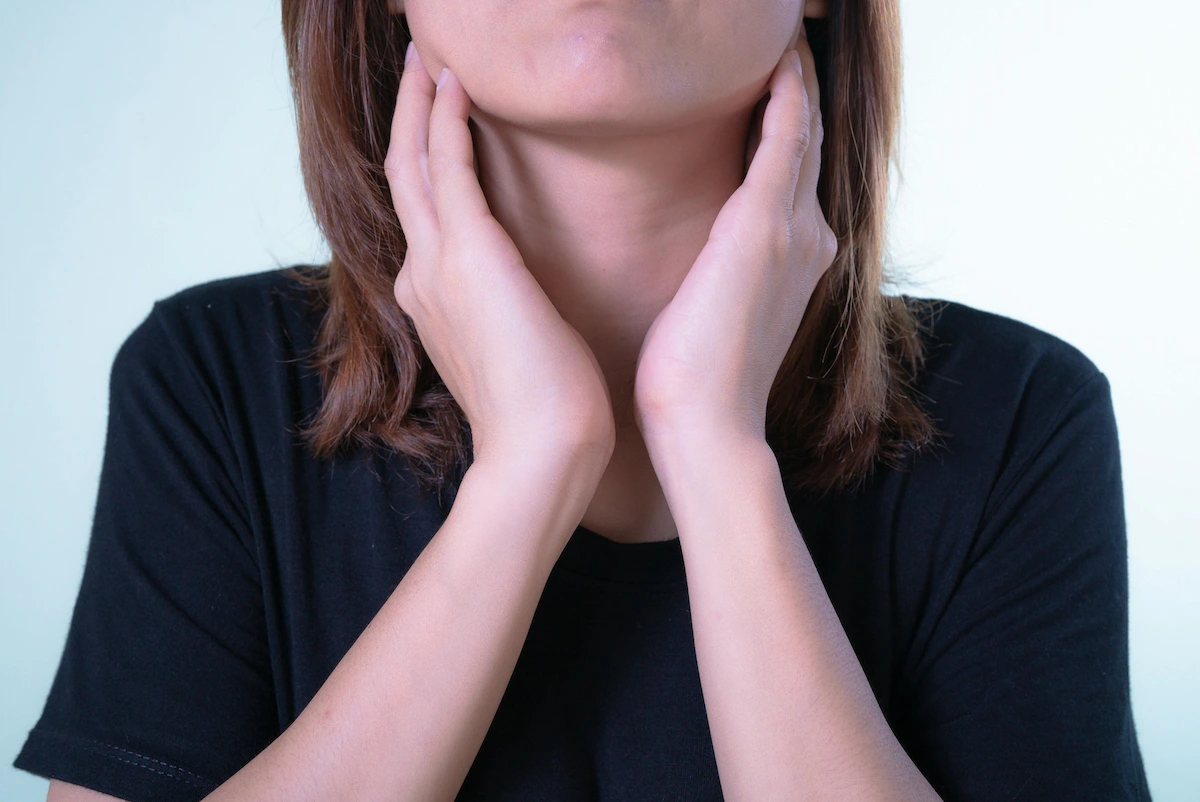 Close-up of a person with hands on their neck, wearing a black t-shirt.