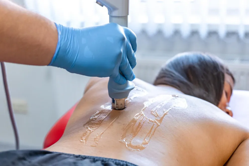 A gloved hand applies a medical device to a person's back, which is covered in clear gel.