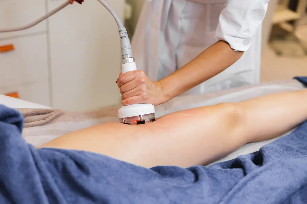 A handheld treatment device being applied to a person's leg, which is partially covered by a blue towel.