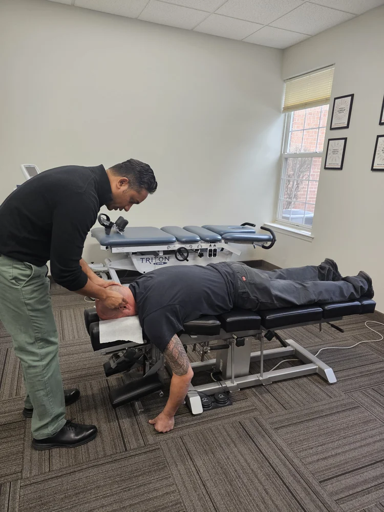 A chiropractor adjusts a male patient's neck who is lying face down on a chiropractic table.