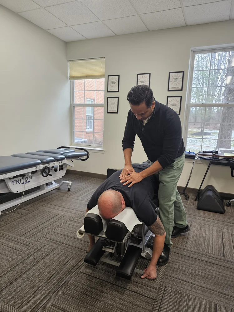 A chiropractor adjusts a patient's back on a chiropractic table in a clinic room.