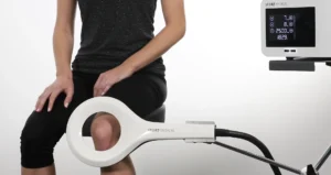 A person seated with a white Storz Medical device around their knee, connected to a unit with a digital display showing settings.