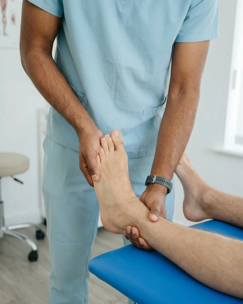 A chiropractor in blue scrubs examines a patient's foot and ankle on a blue examination table.