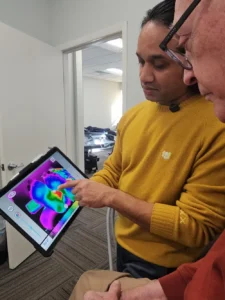 Two men looking at a tablet displaying a thermal image. One man points to the screen.