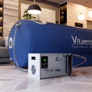 A blue Vitaeris hyperbaric chamber connected to a white air compressor unit with a green light, placed on a wooden floor in a modern room.