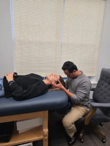 A man performing a manual therapy technique on a woman's head as she lies on an examination table.