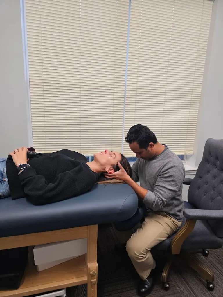 A man performing a manual therapy technique on a woman's head as she lies on an examination table.